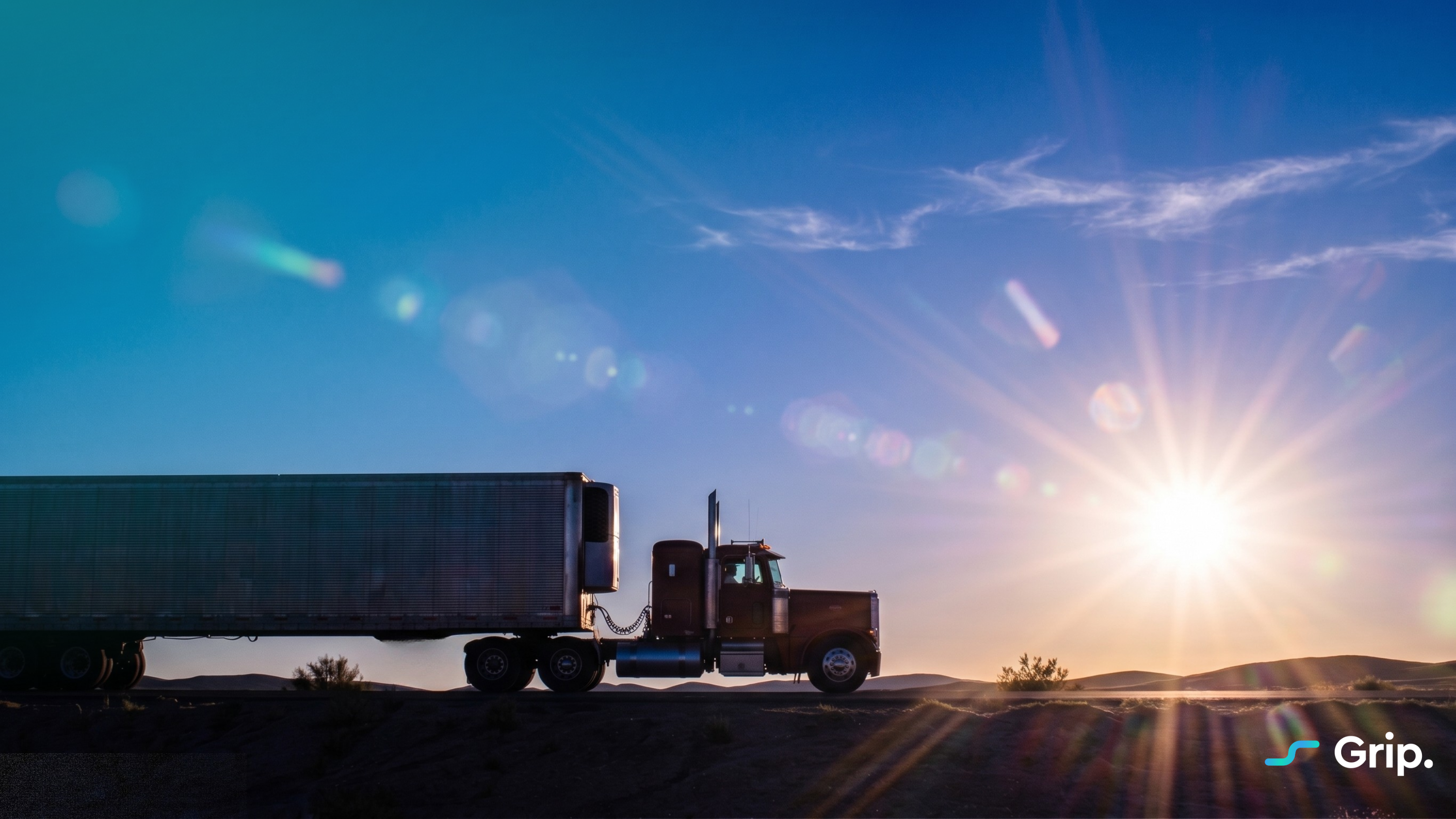 "A truck drives on a desert road at sunrise, casting a silhouette against the bright sun. Grip logo in the corner."